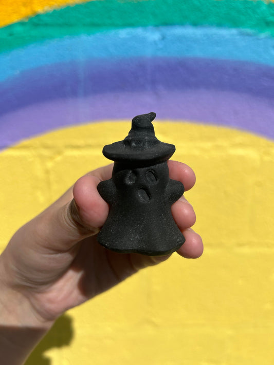 Hand holding black obsidian wizard ghost carving with colorful rainbow background