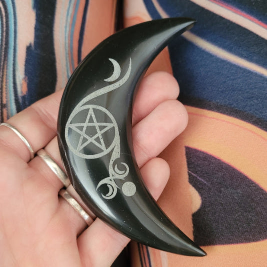 Hand holding black onyx crescent moon with engraved pentacle and mystical symbols, perfect for witch altar rituals