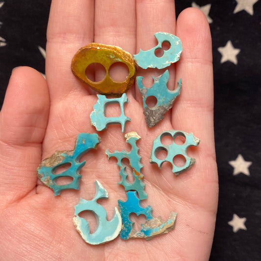 Hand holding irregularly shaped turquoise slab pieces with holes on a star-patterned background
