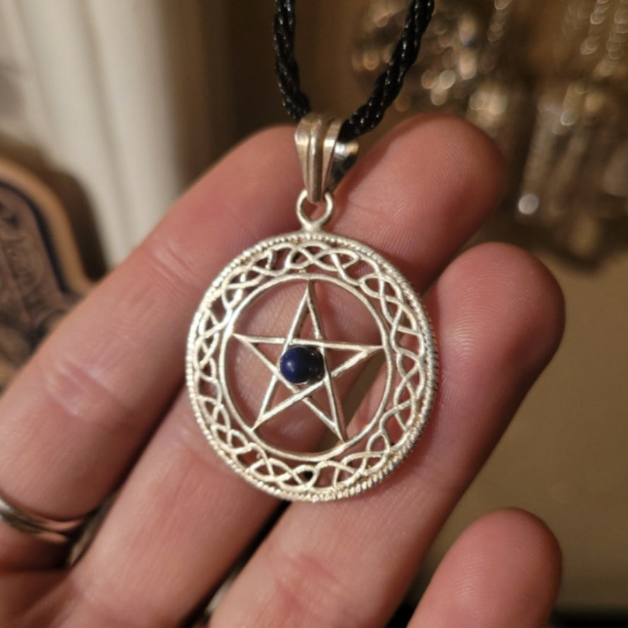 Silver pentacle pendant with blue center stone on black cord necklace held in hand