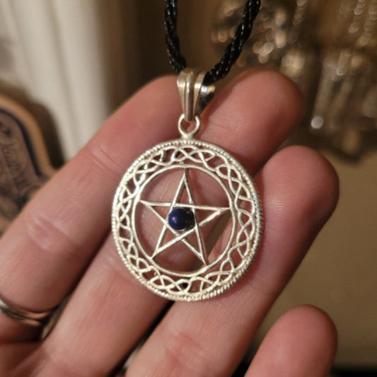 Silver pentacle pendant with blue center stone on black cord necklace held in hand
