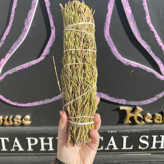 Hand holding a tightly bound Rosemary Smudge Bundle against a dark background with mystical symbols and gold lettering