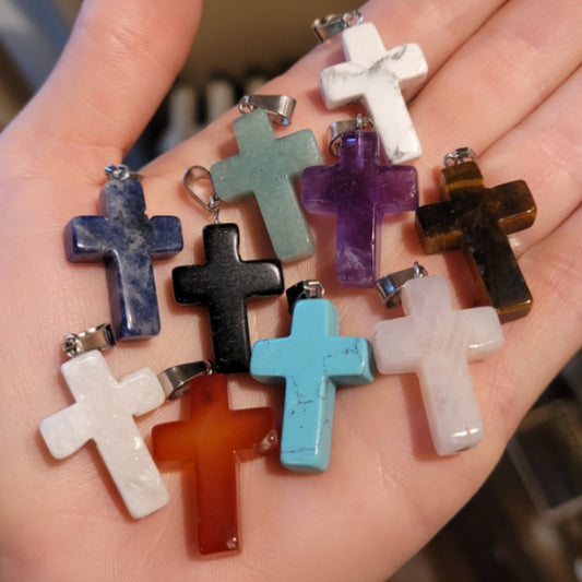 Hand holding assorted colorful crystal cross pendants including carnelian, amethyst, turquoise, and marble variations