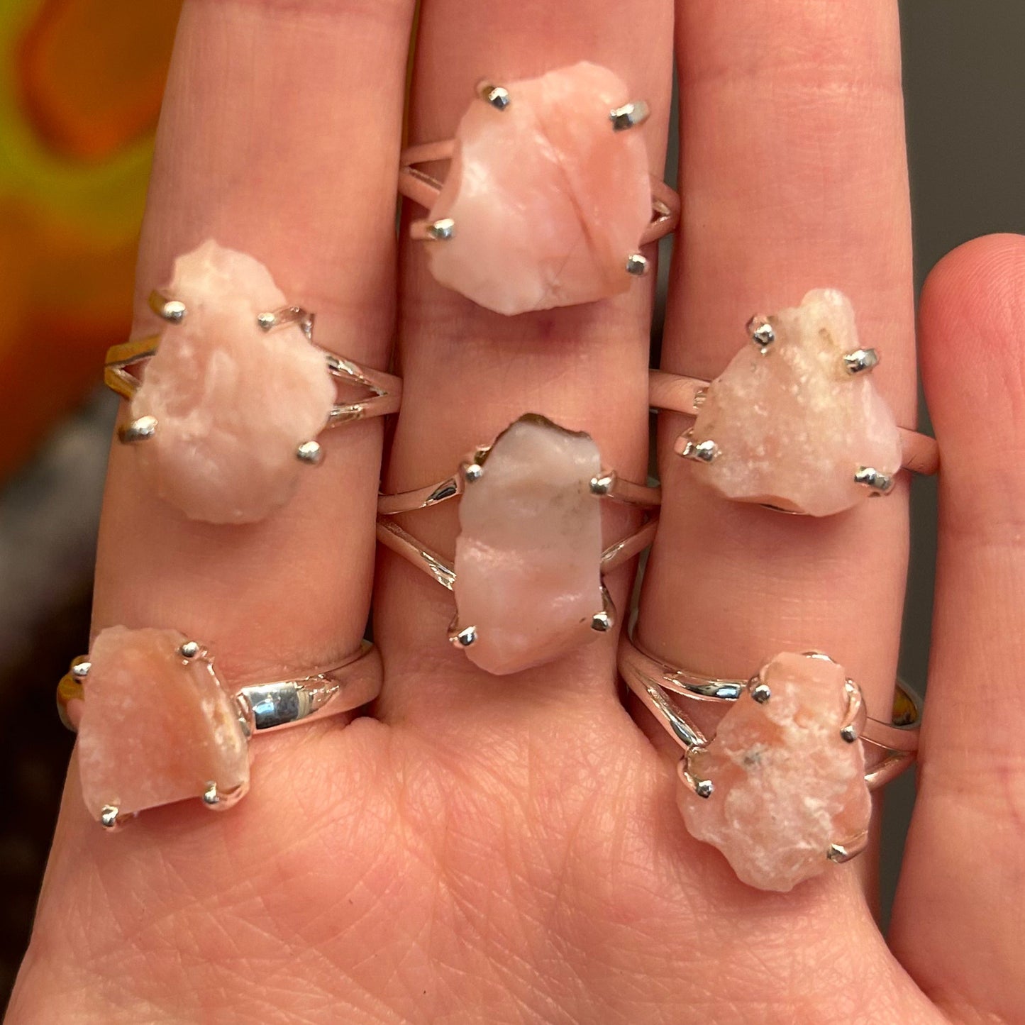close-up of hand wearing multiple pink opal sterling silver rings with raw pink stones
