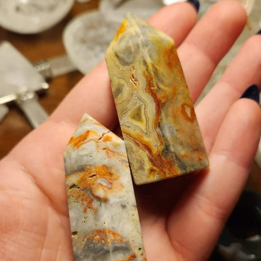 Hand holding two polished Crazy Lace Agate Towers with orange, gray, and beige patterns