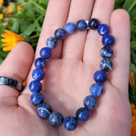 Sodalite bracelet 8mm blue round beads on hand with green and yellow floral background