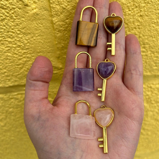 Hand holding three lock and key pendant sets with heart-shaped keys and gold accents against a yellow textured background
