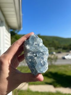 Hand holding a raw blue Celestite Cluster crystal outdoors with a blurred natural background